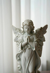 Fototapeta premium Spirituality and prayer concept, stone angel statue with folded hands for meditation, peace and religious devotion in a serene home interior setting