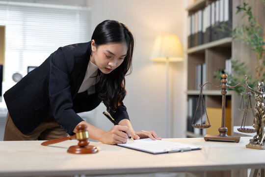 Young female attorney intently reviewing legal paperwork at her office desk.