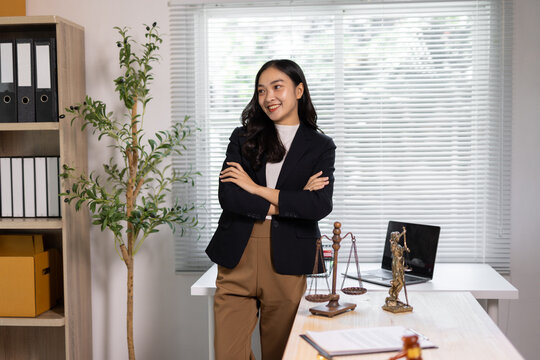 Asian woman lawyer standing in legal office. Professional Asian woman lawyer smiling, standing with crossed arms in a legal office setting, representing justice and law.