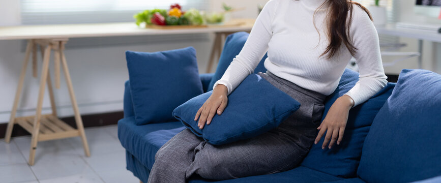 Woman relaxing on blue sofa enjoying comfort at home. Young woman relaxing on a blue sofa in a modern, minimalist living room, cuddling a cushion and enjoying peaceful downtime.