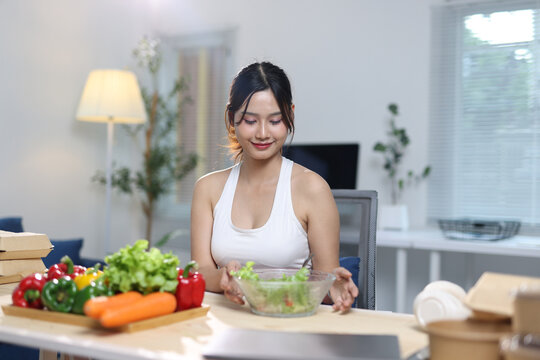 Woman preparing healthy vegetable salad for diet. Young woman smiling while adding ingredients to a fresh vegetable salad, promoting a healthy lifestyle and proper nutrition.