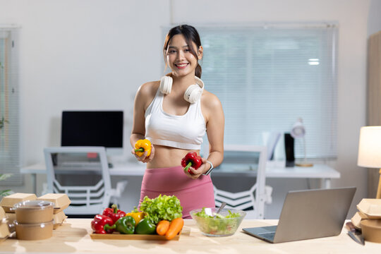 Woman preparing healthy salad for fitness meal prep. Woman in athletic wear holding bell peppers, preparing a fresh salad with vegetables and meal prep containers at home.