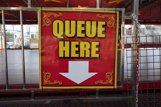 Red and yellow Queue Here sign with arrow on a ride barrier