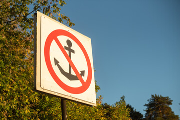 A no anchoring sign with a red circle and diagonal line over an anchor symbol. The background features trees and a clear blue sky, providing ample copy space. © Ksu