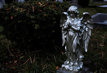 Fototapeta premium Grief and mourning concept, silver angel statue praying at a cemetery grave, religious memorial and funeral tribute in a quiet garden setting