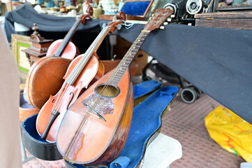 Close-up shot of an antique wooden mandolin resting in an open case alongside classic violins on a market stall filled with vintage collectibles. © pedro