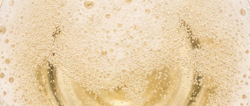 Macro texture of golden champagne bubbles. Sparkling wine fizz in pale yellow liquid. Festive holiday celebration background