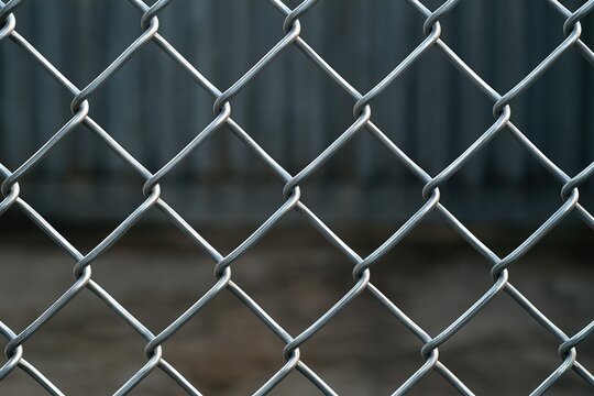 Close up view of a metallic chain link fence with a repeating diamond pattern and dark background
