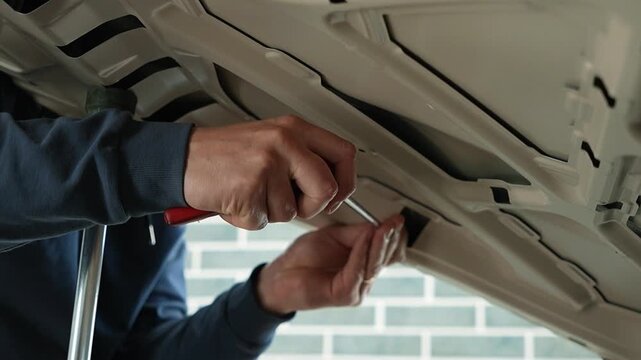 PDR technician in the process of repairing a dent from the inside of a car hood. Professional worker using special metal rod lever tool to fix automotive body panel damage with paintless dent removal.