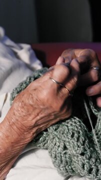 GENOA, ITALY - September 23, 2026. Close-up of an elderly woman's weathered hands skilfully crocheting with a hook, working sparkly green yarn into a textured stitch pattern. Shot indoors in warm ligh