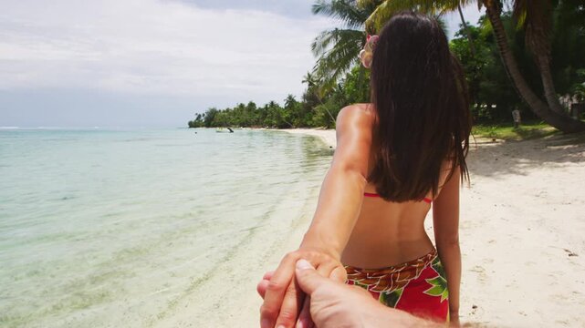 Couple on honeymoon vacation travel holding hands walking on beach. Follow me POV of beautiful woman relaxing on paradise beach on Tahiti, French Polynesia. Video of real woman without any makeup