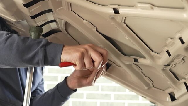 PDR technician in the process of repairing a dent from the inside of a car hood. Professional worker using special metal rod lever tool to fix automotive body panel damage with paintless dent removal.