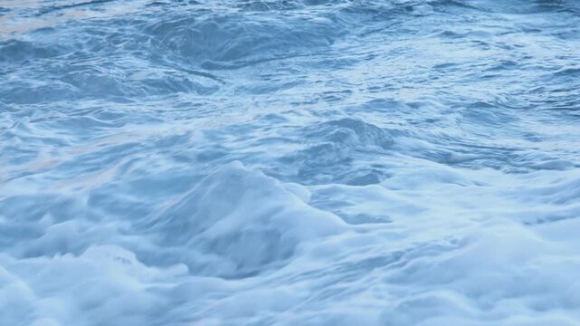 Ocean waves wash over smooth dark volcanic stones on a rugged beach, Madeira, Portugal