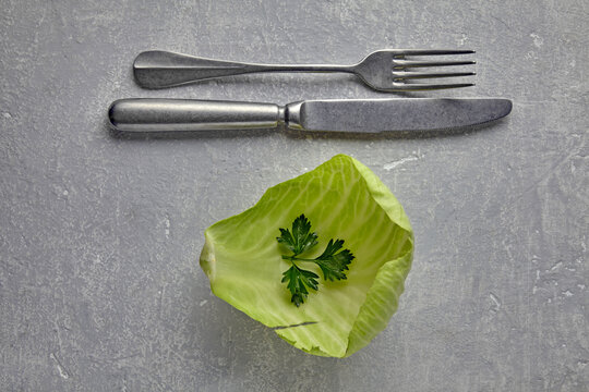 Concept of Dieting with Cabbage Leaf and Cutlery on Grey