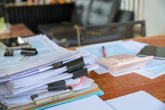 Stack of documents with black clips, calculator, tax form, and pencil placed on home office desk. Business and Financial Planning Concept. Financial advisor plan, use calculator to calculate budget.