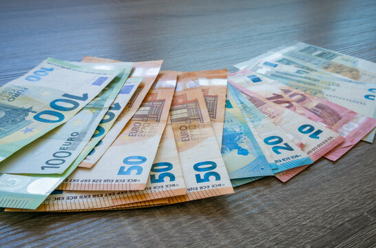 Assorted euro banknotes in ten, twenty, fifty, one hundred and two hundred denominations spread across a dark wooden tabletop