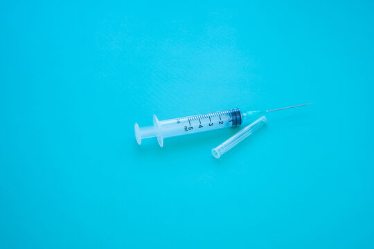 Transparent graduated syringe with needle and detached protective cap on a bright turquoise surface, featuring visible milliliter measurement markings