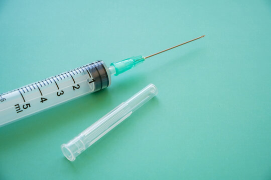 Graduated medical syringe with attached needle beside a transparent protective cap on a turquoise surface, with measurement markings and open space