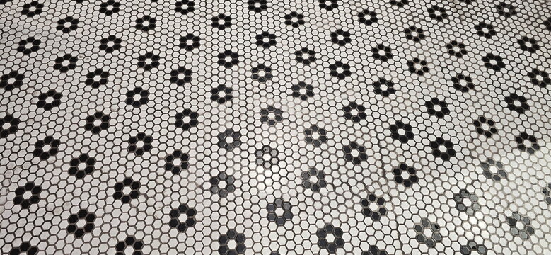 Ceramic tile flooring featuring a black-and-white hexagonal mosaic pattern interspersed with floral motifs. Hexagon . Seamless honeycomb pattern. Small hexagonal white tiles are joined together. 
