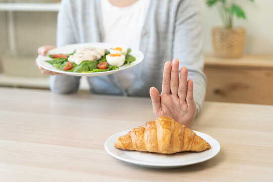 Ketogenic, Low carb, Intermittent Fasting diet woman push out, deny hand push out, deny butter croissant bread on plate, choose green vegetable salad, eat food for good healthy, getting weight loss.