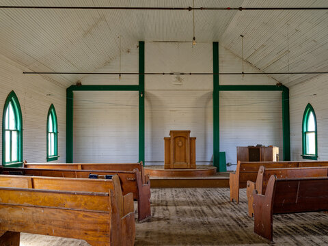 Light shines through the arched windows inside an abandoned country church