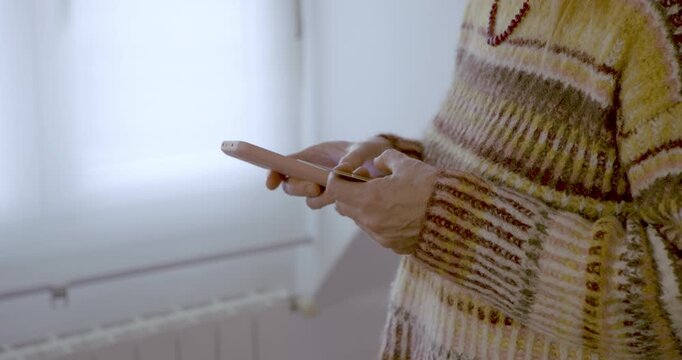 Woman shopping with her card and a smartphone: Close-up of a woman&rsquo;s hands holding a card and a smartphone; her fingers deftly navigate the touchscreen whilst she wears a comfortable, patterned jumper