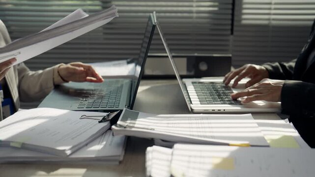 Business Professionals Working on Laptops with Heavy Paperwork at Office Desk