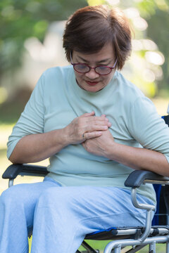 Senior Asian woman sitting on wheelchair suffering from chest pain and heart attack in park