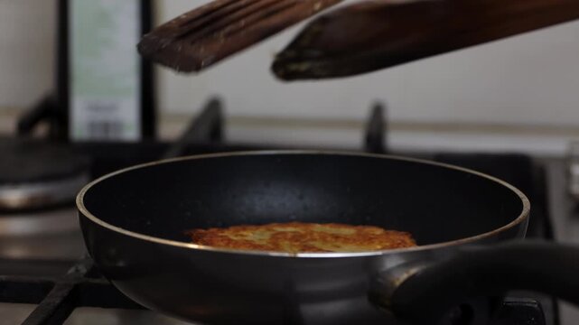 Flipping a crispy yellow split pea patty with wooden spatulas in a frying pan