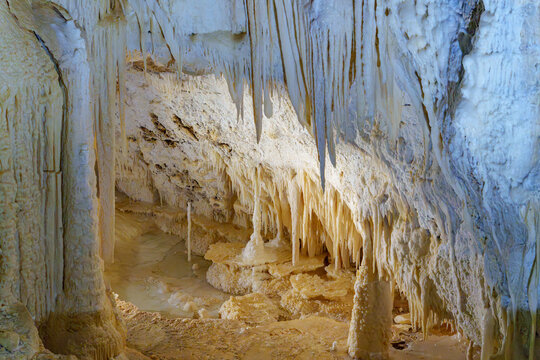 Stunning cave interior with hanging stalactites. Soft light highlights textures and natural formations. Earthy tones contrast with pale mineral walls. Quiet atmosphere invites wonder and stillness.
