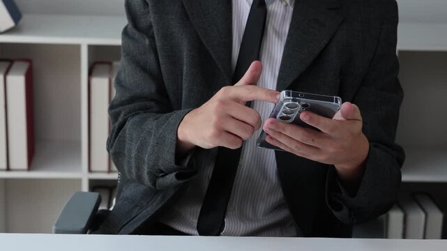 Businessman in a suit using a smartphone at an office desk for communication and online messaging