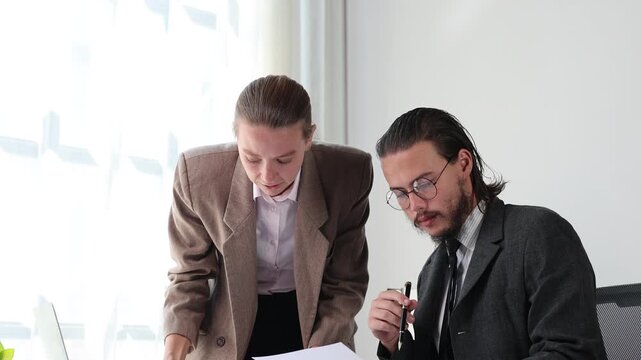 Businesswoman and businessman analyzing data and discussing financial charts during a meeting in a bright corporate office