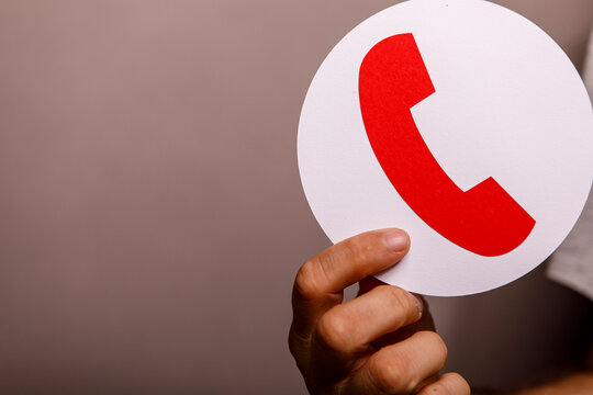 A person holds a white circle with a red telephone receiver symbol, signifying contact or support.
