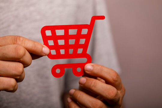 Red shopping cart cutout held by hands, illustrating e-commerce and digital marketing.