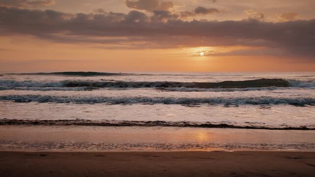 Gentle ocean waves rolling onto a sandy beach shore during a golden sunrise under soft cloudy sky.