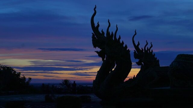 Naga serpent statues silhouette against dramatic colorful sunset sky in Thailand temple