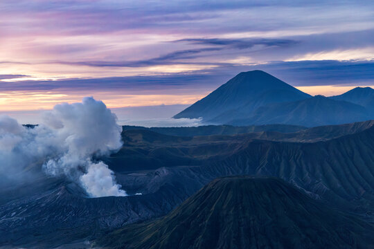 Mount Bromo volcano at sunrise, viewed from King Kong viewpoint in Bromo Tengger Semeru National Park, East Java, Indonesia. Active crater smoke, Mount Semeru cone, clouds, and vast ash plain.