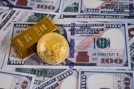 A single physical golden Bitcoin token coin leaning against a fine gold bullion bar on top of a messy spread of US 100 dollar.