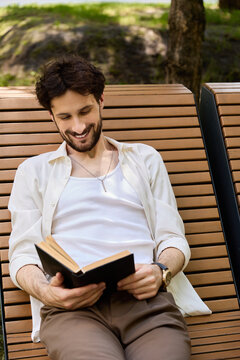 Stylish young man enjoys reading a book in a sunny city park setting
