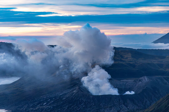 Mount Bromo volcano at sunrise, viewed from King Kong viewpoint in Bromo Tengger Semeru National Park, East Java, Indonesia. Active crater smoke, Mount Semeru cone, clouds, and vast ash plain.