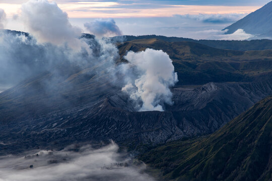 Mount Bromo volcano at sunrise, viewed from King Kong viewpoint in Bromo Tengger Semeru National Park, East Java, Indonesia. Active crater smoke, Mount Semeru cone, clouds, and vast ash plain.
