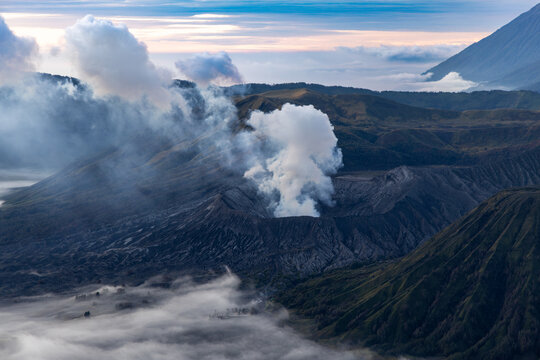 Mount Bromo volcano at sunrise, viewed from King Kong viewpoint in Bromo Tengger Semeru National Park, East Java, Indonesia. Active crater smoke, Mount Semeru cone, clouds, and vast ash plain.