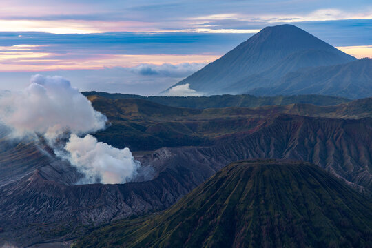 Mount Bromo volcano at sunrise, viewed from King Kong viewpoint in Bromo Tengger Semeru National Park, East Java, Indonesia. Active crater smoke, Mount Semeru cone, clouds, and vast ash plain.