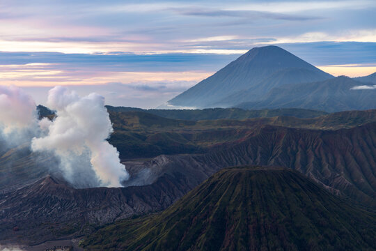 Mount Bromo volcano at sunrise, viewed from King Kong viewpoint in Bromo Tengger Semeru National Park, East Java, Indonesia. Active crater smoke, Mount Semeru cone, clouds, and vast ash plain.