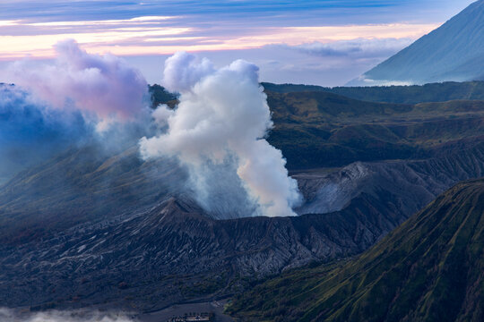 Mount Bromo volcano at sunrise, viewed from King Kong viewpoint in Bromo Tengger Semeru National Park, East Java, Indonesia. Active crater smoke, Mount Semeru cone, clouds, and vast ash plain.