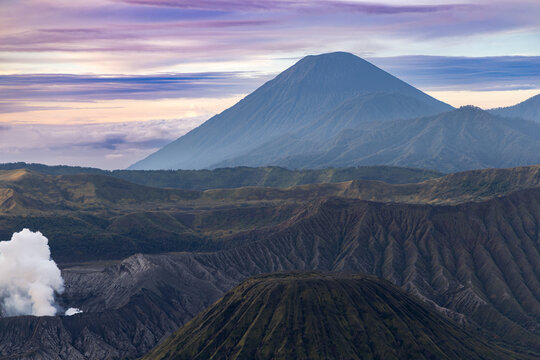 Mount Bromo volcano at sunrise, viewed from King Kong viewpoint in Bromo Tengger Semeru National Park, East Java, Indonesia. Active crater smoke, Mount Semeru cone, clouds, and vast ash plain.