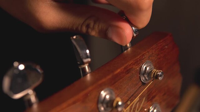 4K close-up shot of a man&rsquo;s hand tuning the knob of a wooden acoustic guitar for the strings. The concept of art, entertainment, creativity, and live performance.