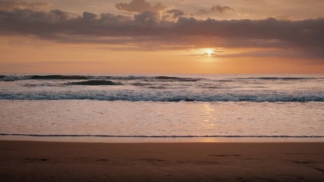 Gentle ocean waves rolling onto a sandy beach shore during a golden sunrise under soft cloudy sky.