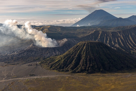 Mount Bromo volcano at sunrise, viewed from King Kong viewpoint in Bromo Tengger Semeru National Park, East Java, Indonesia. Active crater smoke, Mount Semeru cone, clouds, and vast ash plain.