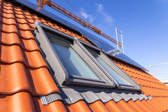 K&uuml;rzlich eingedecktes Ziegeldach mit Dachfenstern und Solarpaneelen an einem neuen Einfamilienhaus